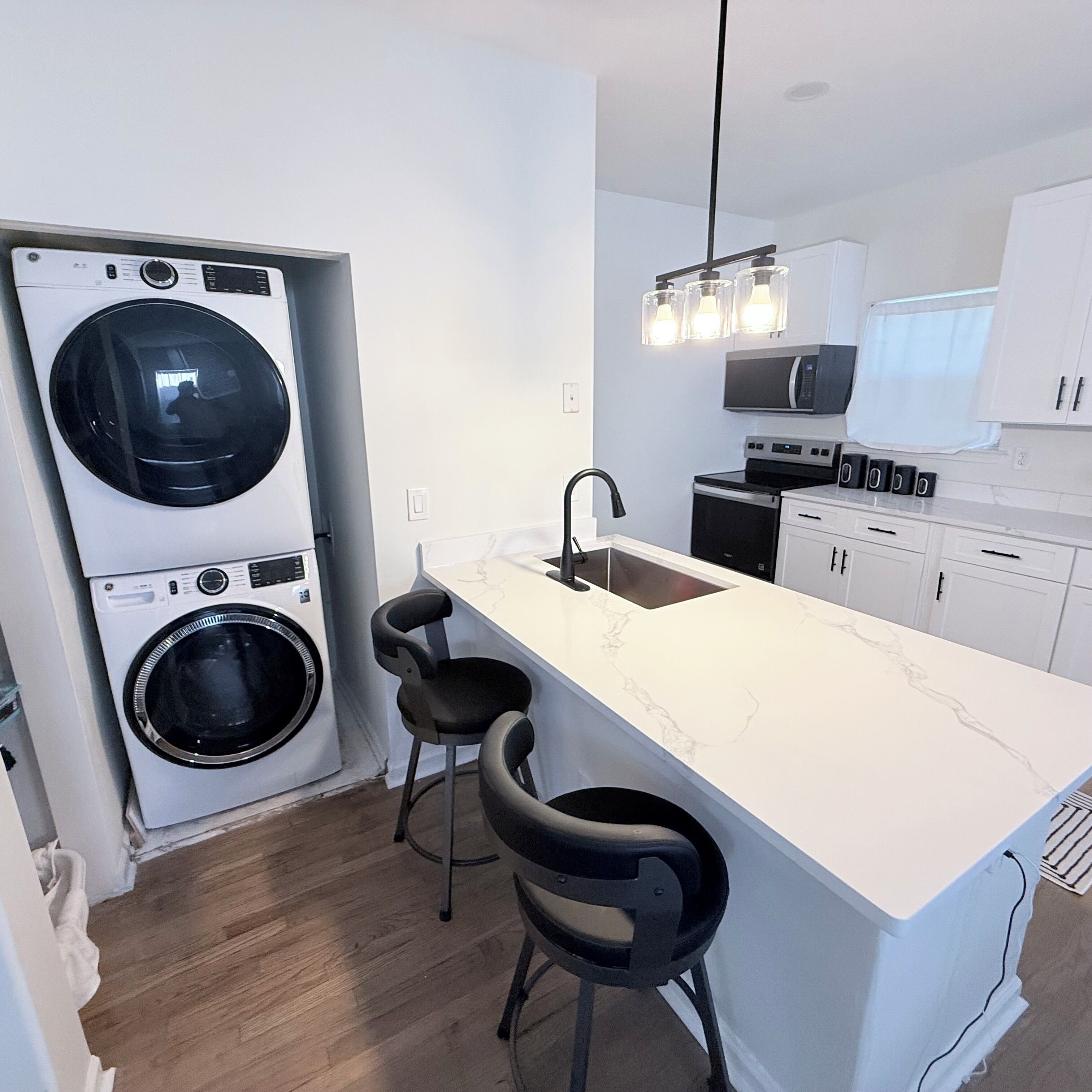 Une cuisine compacte équipée d’un lave-linge intégré, d’un évier et d’un coin bar avec des tabourets.