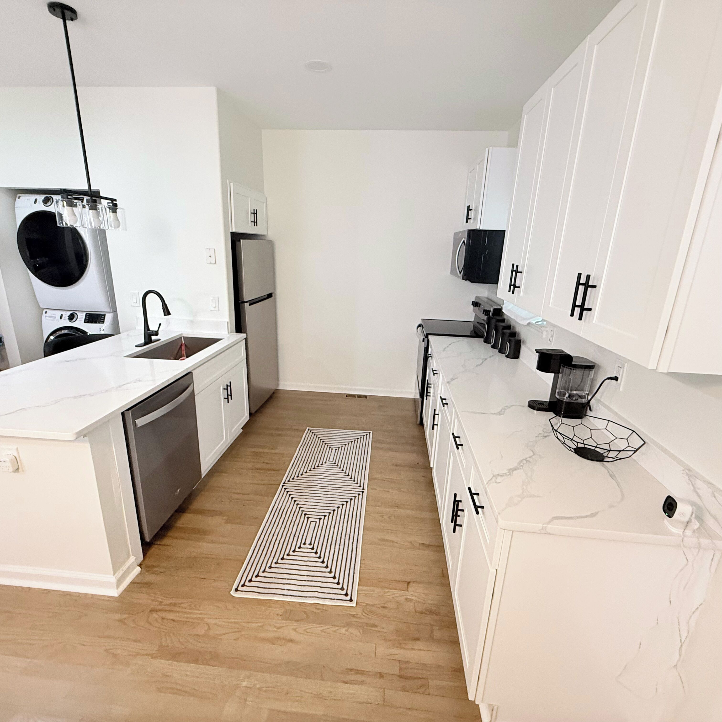 A modern kitchen with white cabinetry, a built-in washing machine, a refrigerator, and a marble countertop.