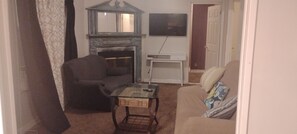 Un salon avec une cheminée, un téléviseur fixé au mur, un canapé et une table basse.