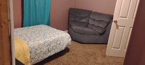 A bedroom with a bed, a gray armchair, and a closed door.