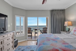 A hotel room with a bed, a TV, a desk, a lamp, and a view of the beach. - Luxury 4 BR Beachfront Condo - Admirals Quarters 601A - Indoor Outdoor Pool (Orange Beach)