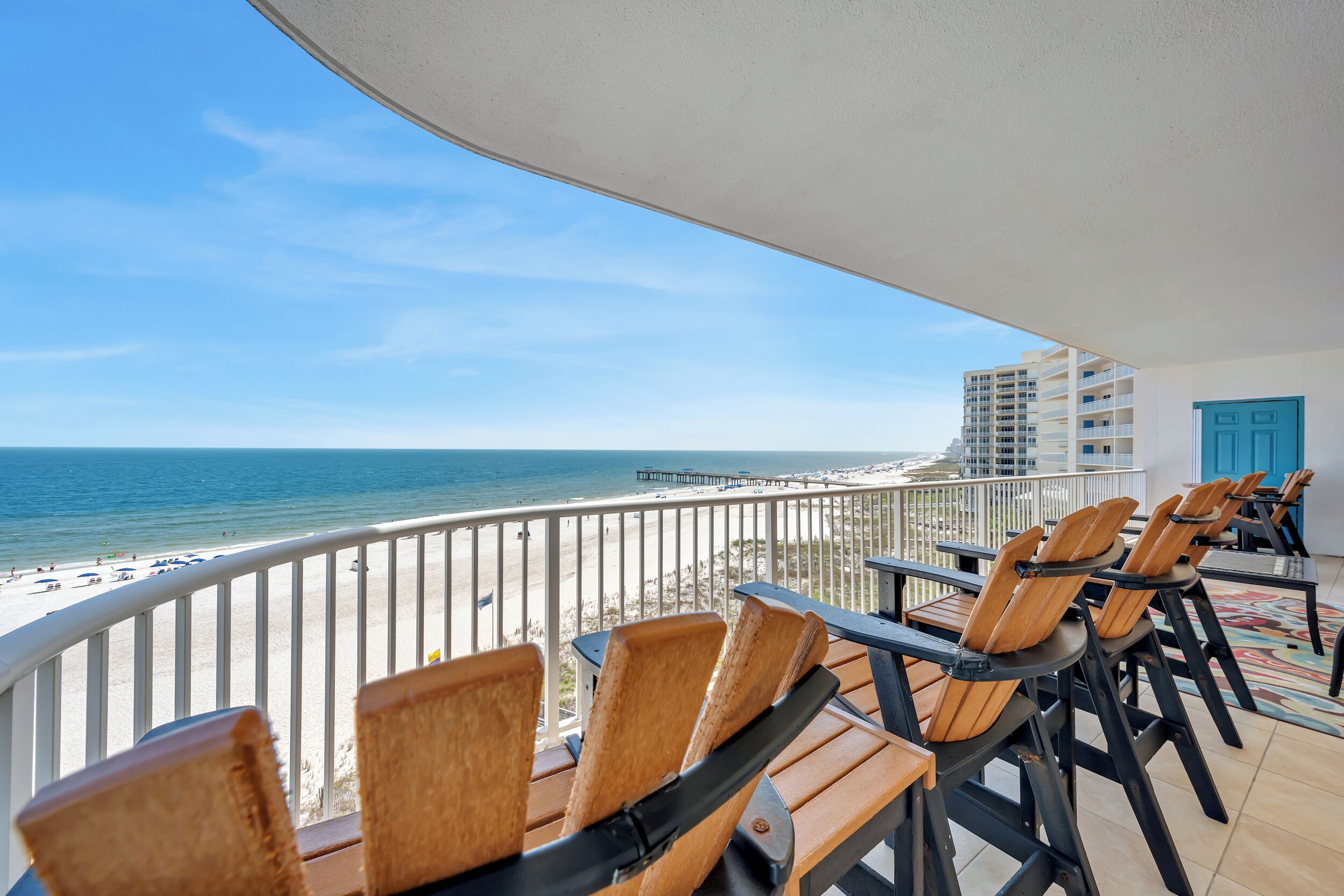 A balcony with wooden chairs and a view of the beach and ocean.
