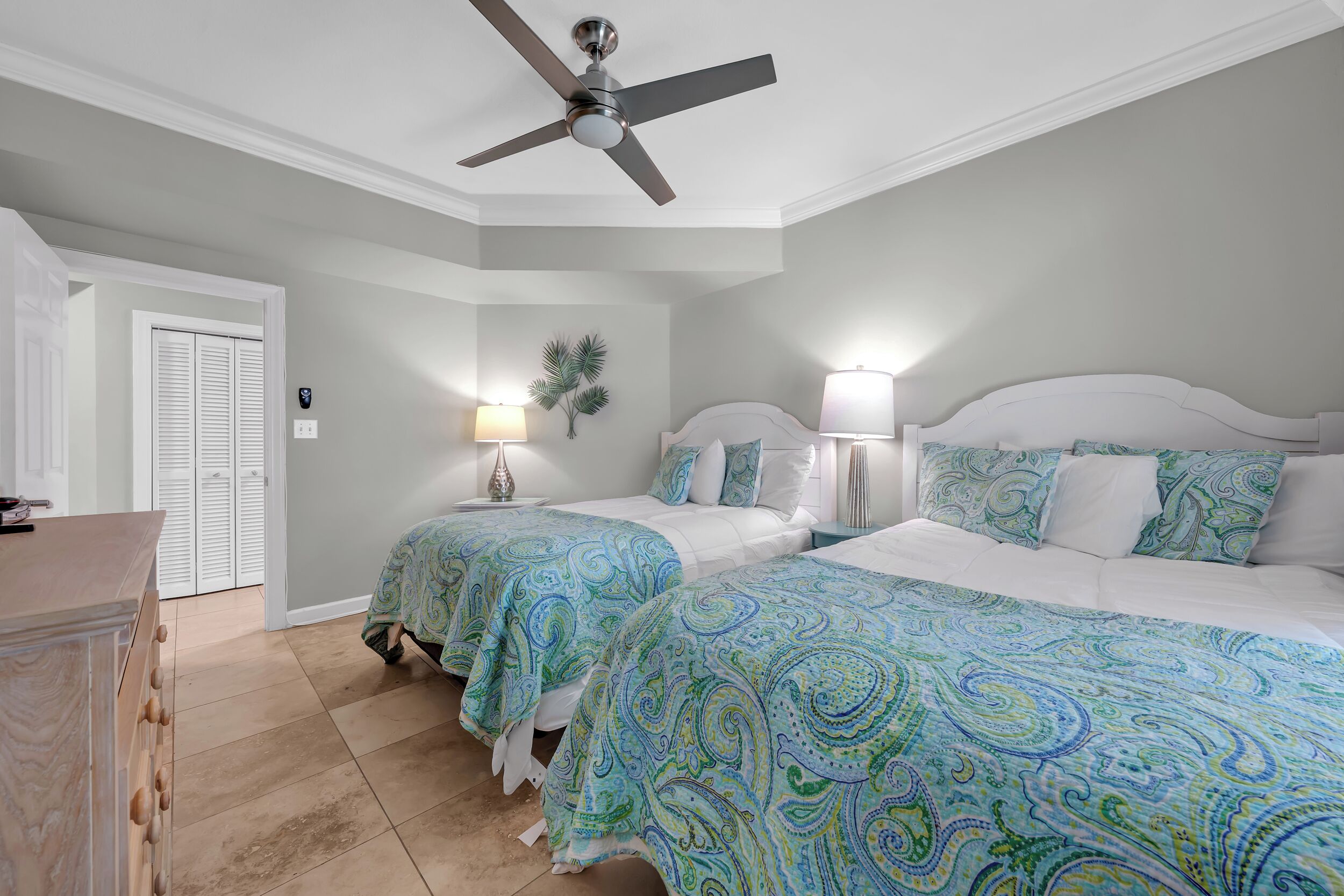 A bedroom with two beds, a ceiling fan, bedside lamps, a wall-mounted plant, and a door with a white closet.