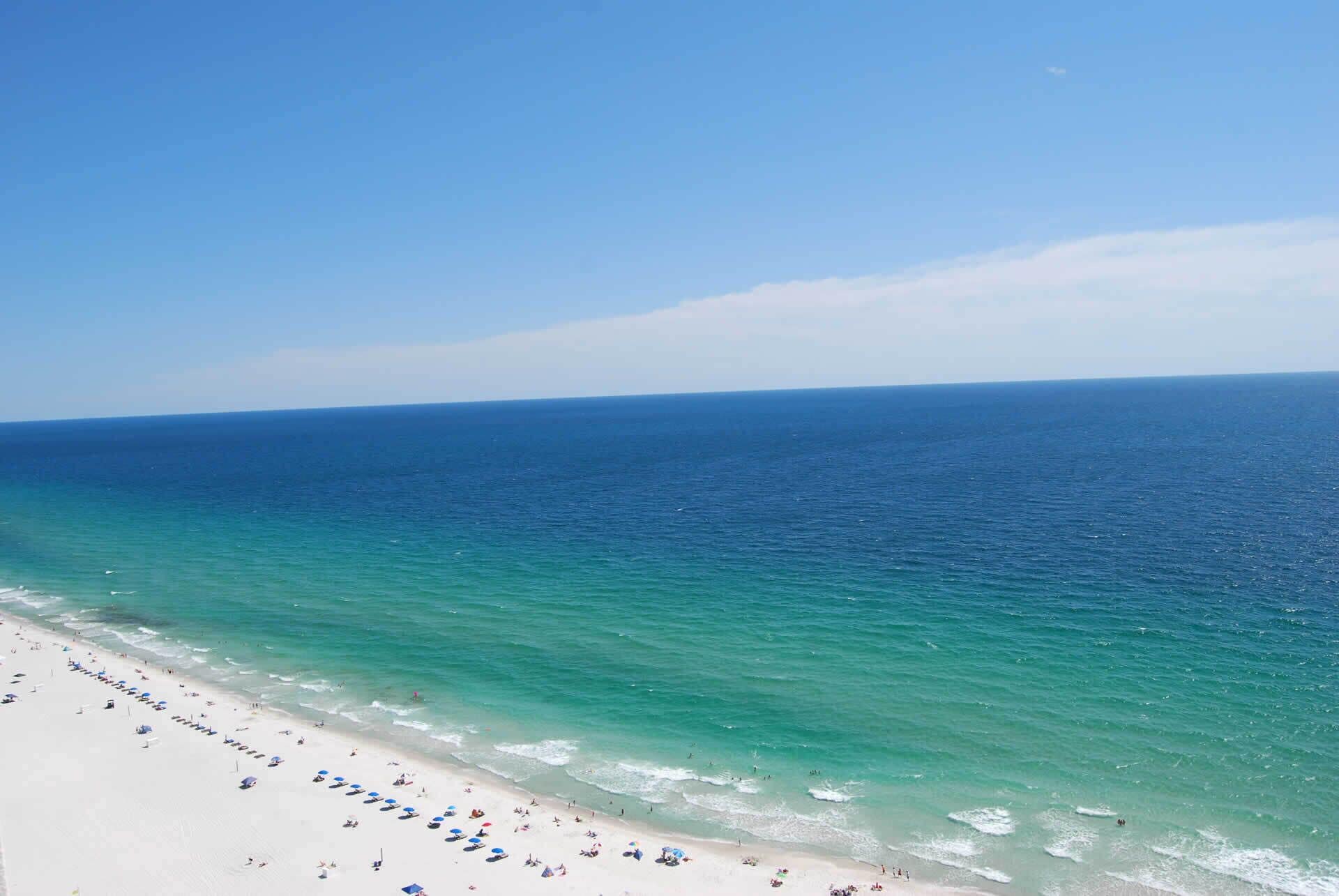 A beach with clear blue water, white sand, and umbrellas.