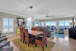 A spacious living area with a dining table, chairs, a sofa, and a view of the ocean. - Luxury 4 BR Beachfront Condo - Admirals Quarters 601A - Indoor Outdoor Pool (Orange Beach)