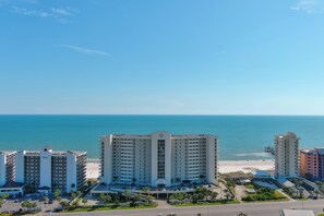 Un hôtel de grande hauteur doté d’un atrium central, offrant une vue sur la plage et disposant d’un parking agrémenté de palmiers.