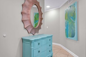 A hallway with a light blue dresser, a decorative mirror, and a large abstract painting on the wall. - Luxury 4 BR Beachfront Condo - Admirals Quarters 601A - Indoor Outdoor Pool (Orange Beach)