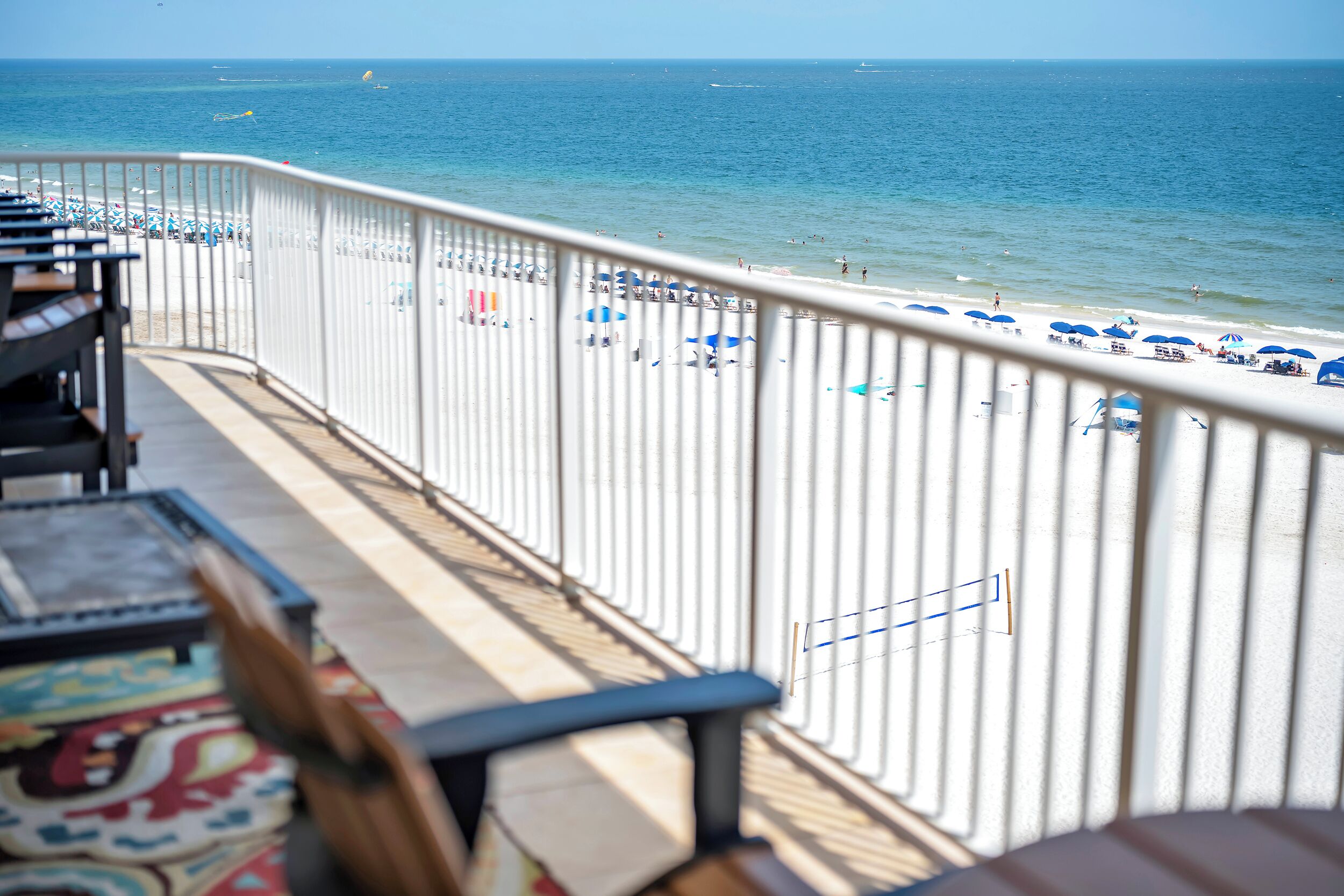 Ein Balkon mit Blick auf einen Strand, einem Geländer und einem Tisch mit gemustertem Tischlein.
