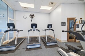 Ein Fitnessraum mit drei Laufbändern, einer Wanduhr, einem Ventilator und einer Tür mit einem Schild.
