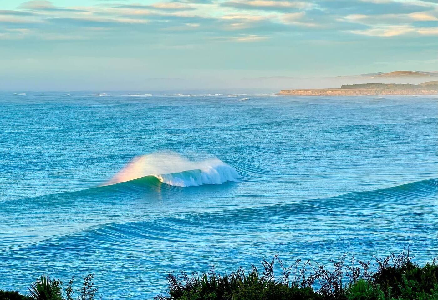 A coastal landscape with a wave in the ocean and a distant landmass.