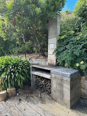 An outdoor barbecue area with a stone-built grill, surrounded by lush greenery.
