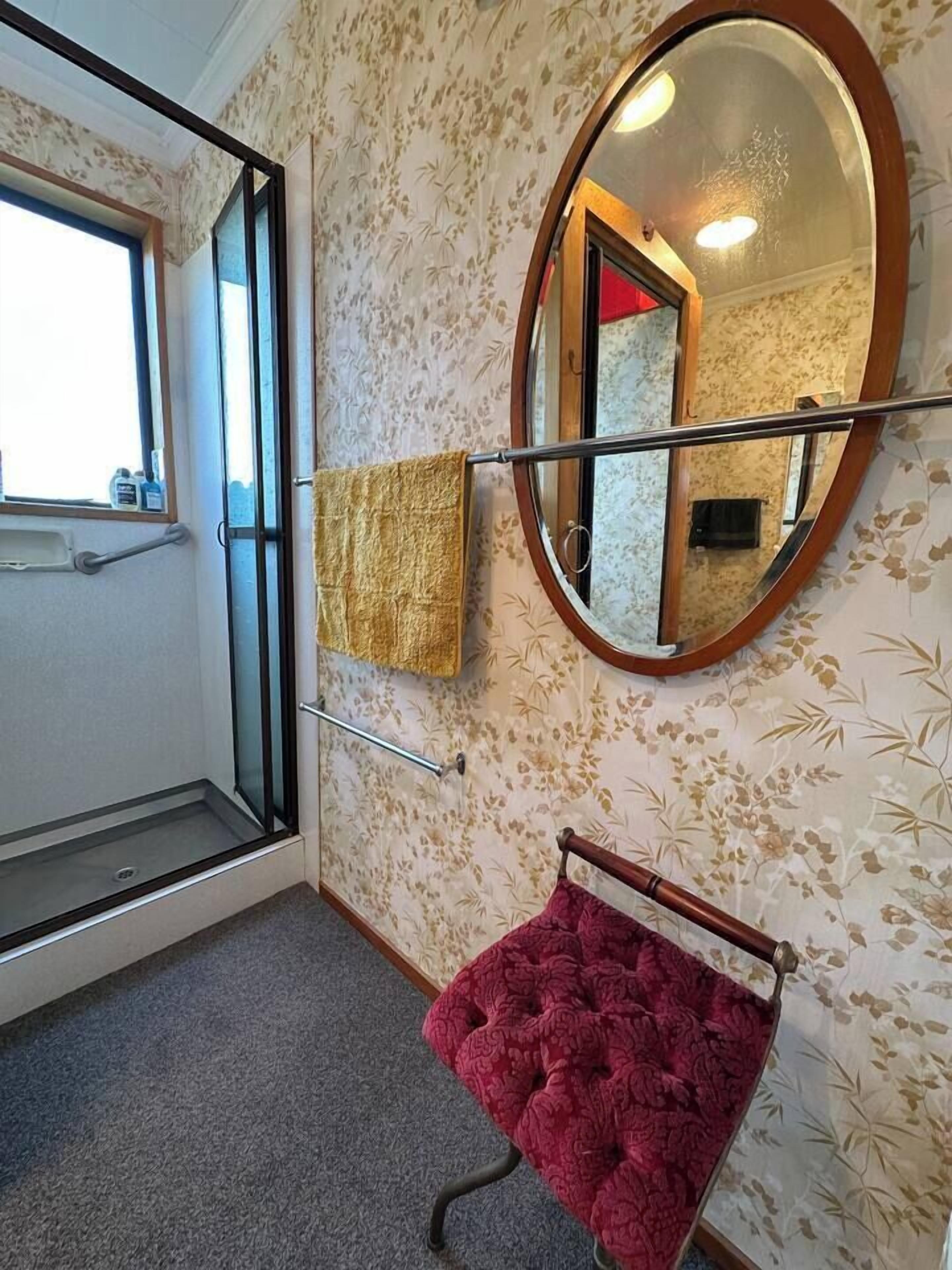 A bathroom with a shower, a mirror, and a red bath mat.