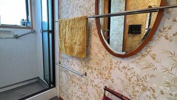A bathroom with a shower, a mirror, and a red bath mat.