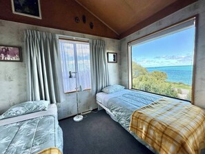 Ein Zimmer mit zwei Betten, einem Vorhangfenster, einem kleinen Tisch und Meerblick.