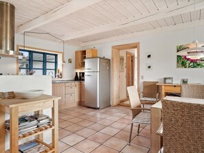 Eine moderne Küche mit einem Edelstahlkühlschrank, Holzschränken und einem Essbereich mit Korbstühlen.