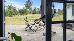 Un patio con mesa y sillas, una parrilla y vistas a un campo cubierto de césped y árboles.