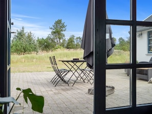 Eine Terrasse mit Tisch, Stühlen, einem Grill und Blick auf ein Wiesfeld und Bäume.