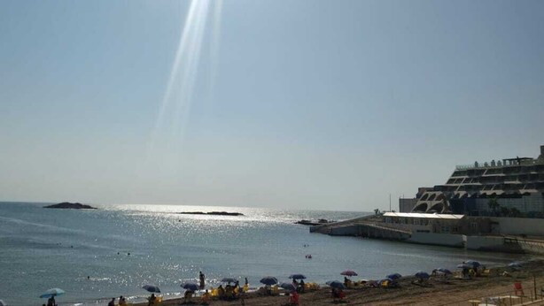 Een strand met een pier, parasols en een heldere lucht.