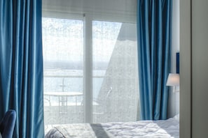 Hotellihuone, jossa on sänky, yöpöytä, lamppu sekä näkymä parvekkeelle ja ulkoalueelle.