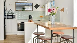 Uma cozinha moderna com armários brancos, uma ilha de madeira com banquetas, um micro-ondas e um vaso com flores.