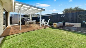 Um quintal com deck de madeira, móveis de jardim e um espaço coberto de varanda.