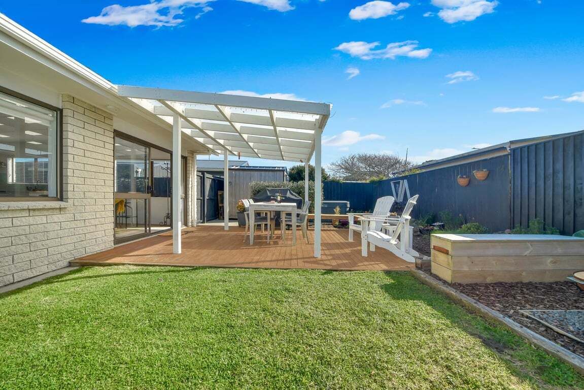 A backyard with a covered patio, a wooden deck, and a grassy lawn.