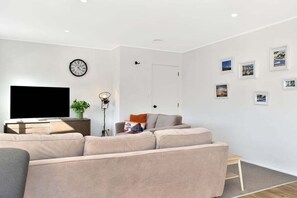 Ein modernes Wohnzimmer mit einem großen Flachbildfernseher, einem beige farbenen Sofa, einer Stehlampe und einer Wanduhr.