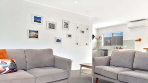 Uma sala de estar moderna com dois sofás cinza, uma pequena mesa e uma área de cozinha ao fundo.