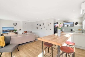 Eine moderne Küche mit Holztisch, Barhocker, einer Couch und einem Fernseher im Wohnbereich.