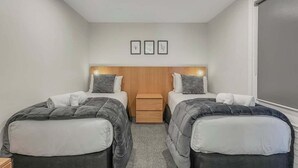 A hotel room with two beds, a wooden headboard, a small bedside table, and a window. - Postcard Views & Pure Comfort: Your Lakeside Haven (Queenstown)