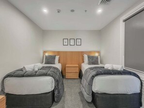 Quarto de hotel com duas camas, uma cabeceira de madeira, uma pequena mesa de cabeceira e uma janela.