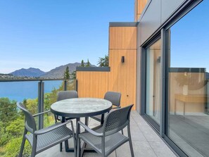 Ein Balkon mit rundem Tisch und Stühlen, mit Blick auf ein Gewässer und Berge.