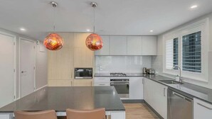 A modern kitchen with a central island, two pendant lights, and a window with blinds. - Postcard Views & Pure Comfort: Your Lakeside Haven (Queenstown)