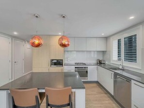 Uma cozinha moderna com ilha central, duas luminárias pendentes e uma janela com persianas.