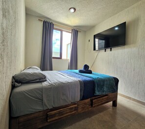 A bedroom with a bed, curtains, a television mounted on the wall, and a window.