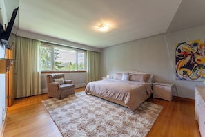 A bedroom with a bed, a chair, a nightstand, a TV, and a painting on the wall.