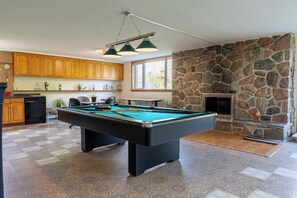 A pool table with surrounding wooden cabinets and a stone fireplace.