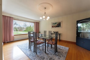 A dining area with a glass table, metal chairs, a patterned rug, a ceiling light fixture, and a window with curtains.