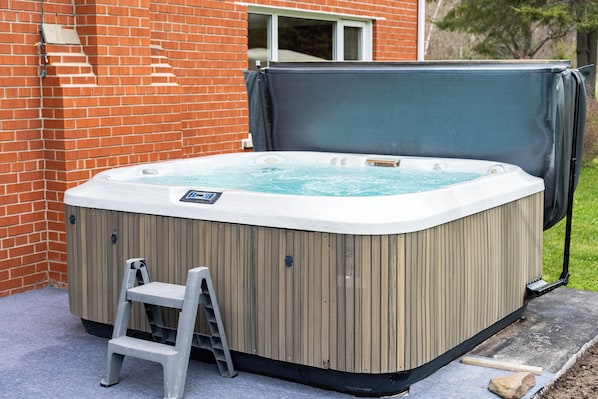 A hot tub with a wooden exterior, a ladder, and a brick wall in the background.