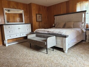 A bedroom with a bed, a dresser, a bench, and a mirror.