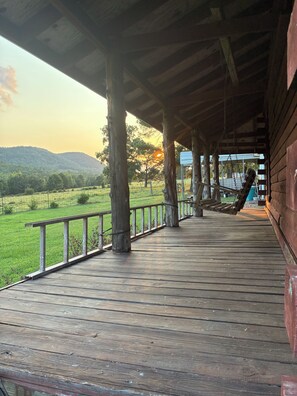 Eine Holzterrasse mit Blick auf ein grünes Feld und Hügel in der Ferne.