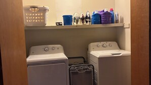 Uma lavanderia com duas máquinas de lavar, um varal e prateleiras com produtos de limpeza.