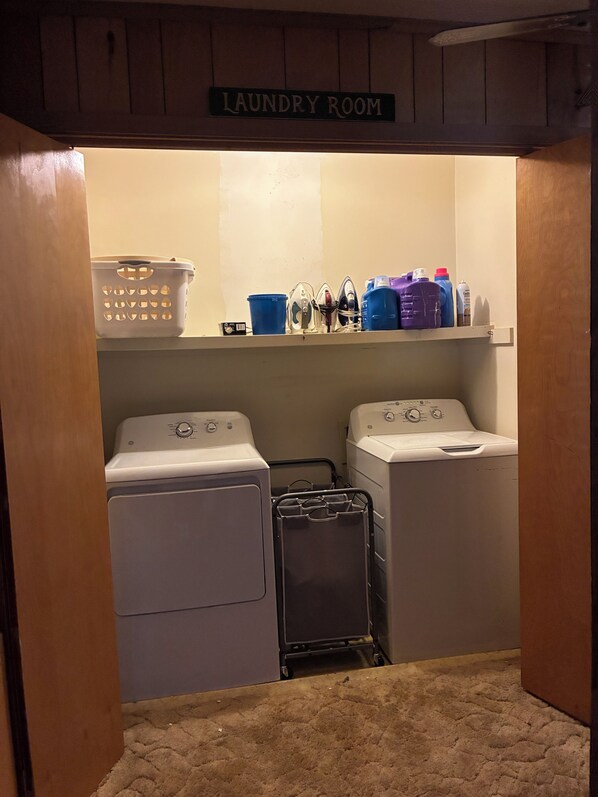 A laundry room with two washing machines, a drying rack, and shelves with laundry supplies.