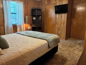 Ein Schlafzimmer mit einem Bett, einem an der Wand befestigten Fernseher und Holzvertäfelung.
