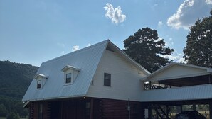 Uma cabana de toras de um andar, com telhado de metal, situada em um campo gramado e paisagem montanhosa.