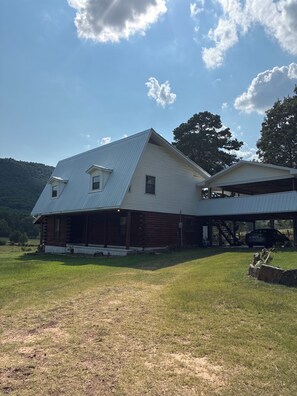 Eine große, eingeschossige Blockhütte mit Metallbedachung, umgeben von einer Wiese und einer hügeligen Landschaft.