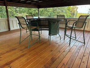 A covered outdoor patio with a wooden deck, a round table, and four chairs.