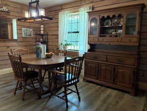 A wooden dining room with a round table, chairs, and a cabinet with glass doors.