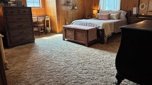 Um quarto acolhedor com piso de madeira, uma cama com dossel, uma cômoda e uma escrivaninha com cadeira.