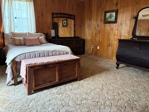 A bedroom with a bed, a dresser, a bench, and a dresser with a mirror.